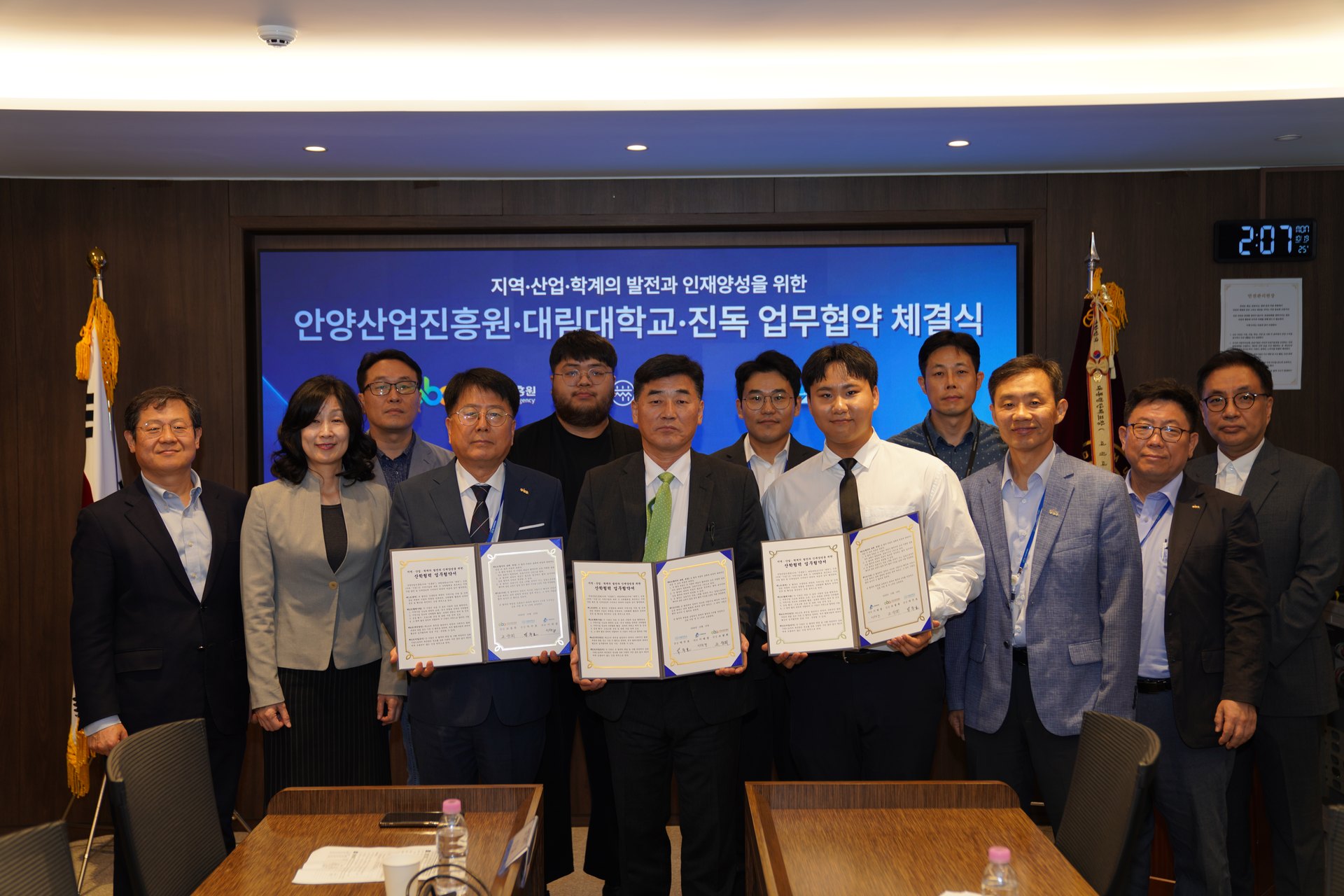 협약 체결식 화면 앞에서 협약서를 든 세 사람을 가운데 두고 참석자들이 두 줄로 서서 기념촬영을 하고 있다